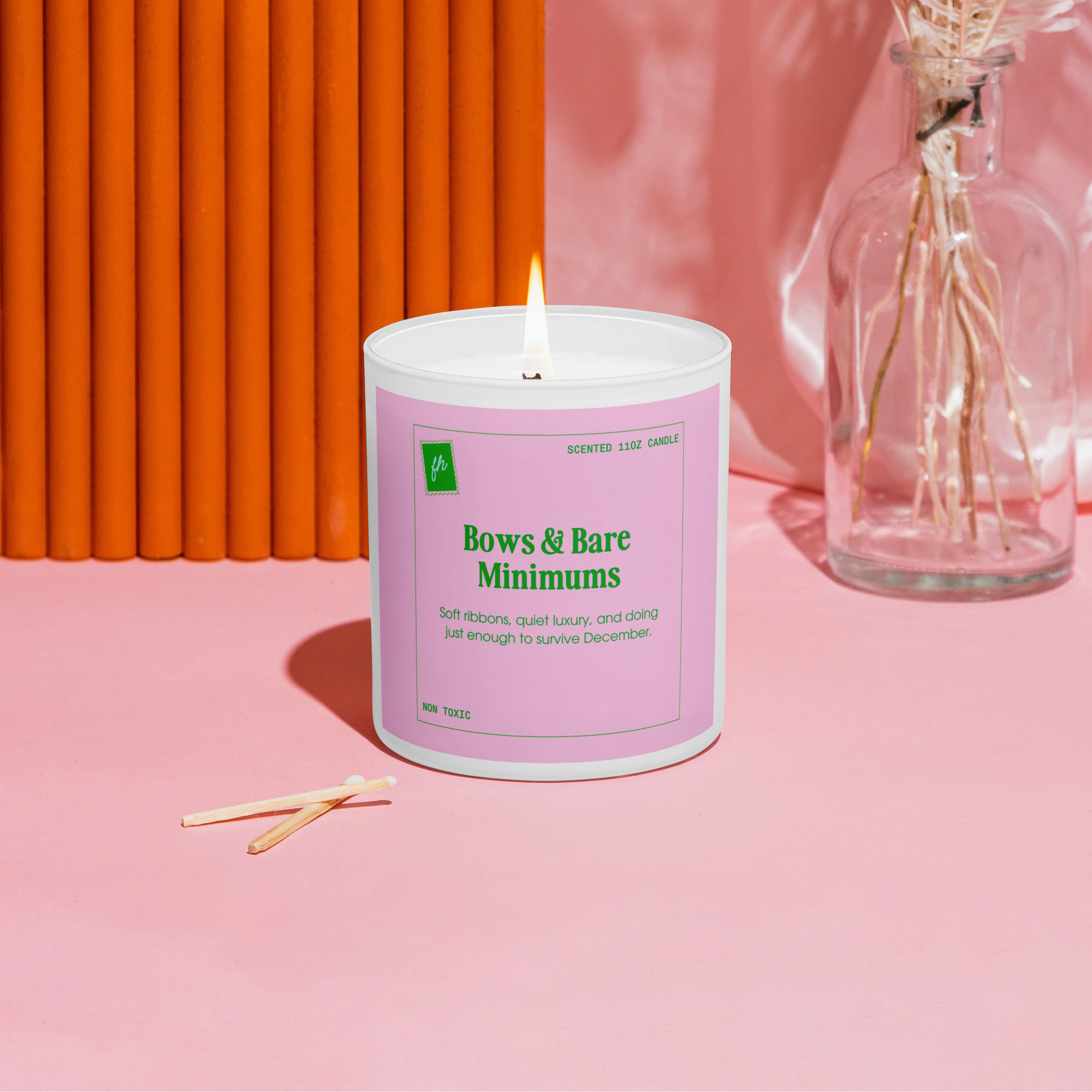Candle with a pink label on a pink surface with an orange wall in the background