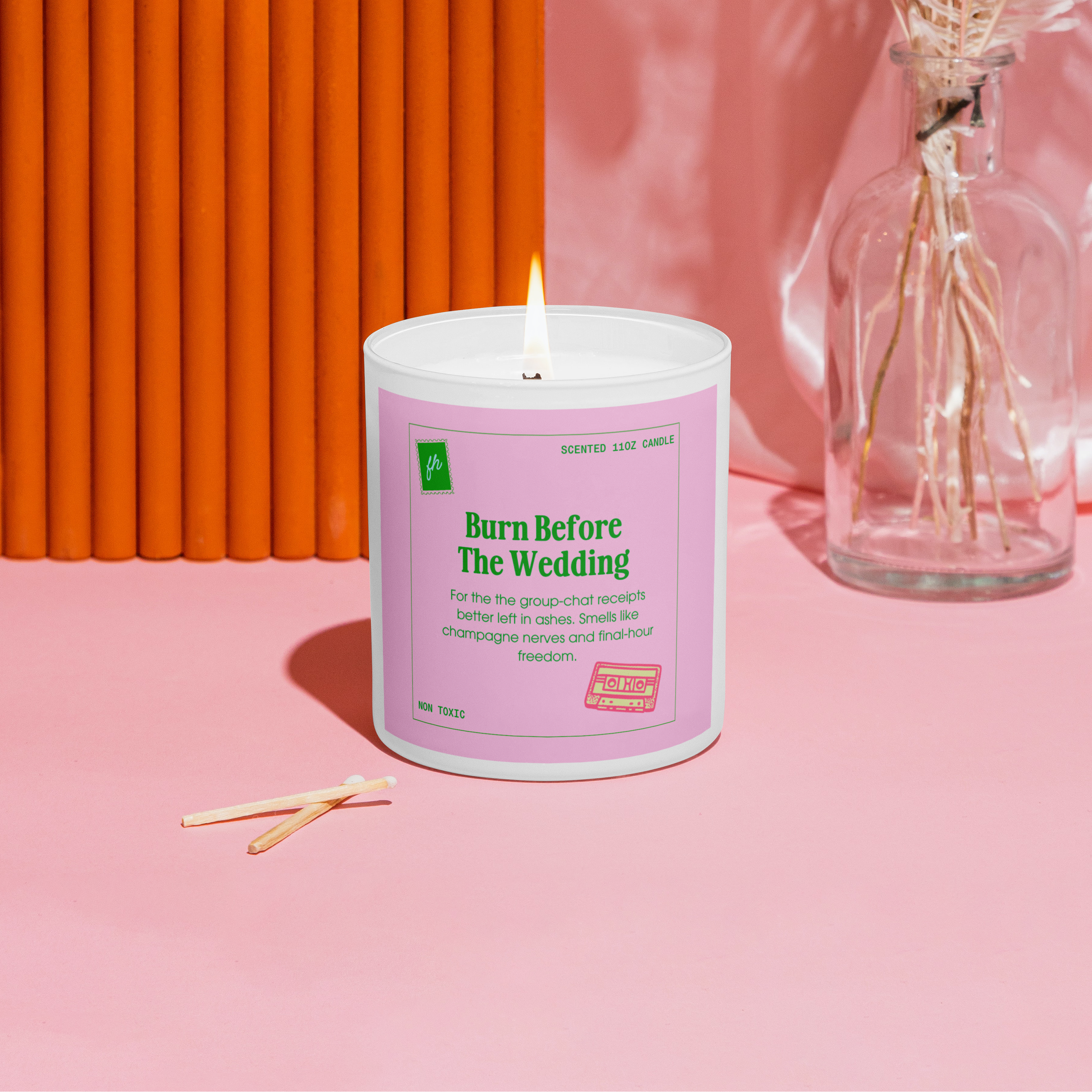 Candle with a pink label on a pink surface with an orange wall in the background