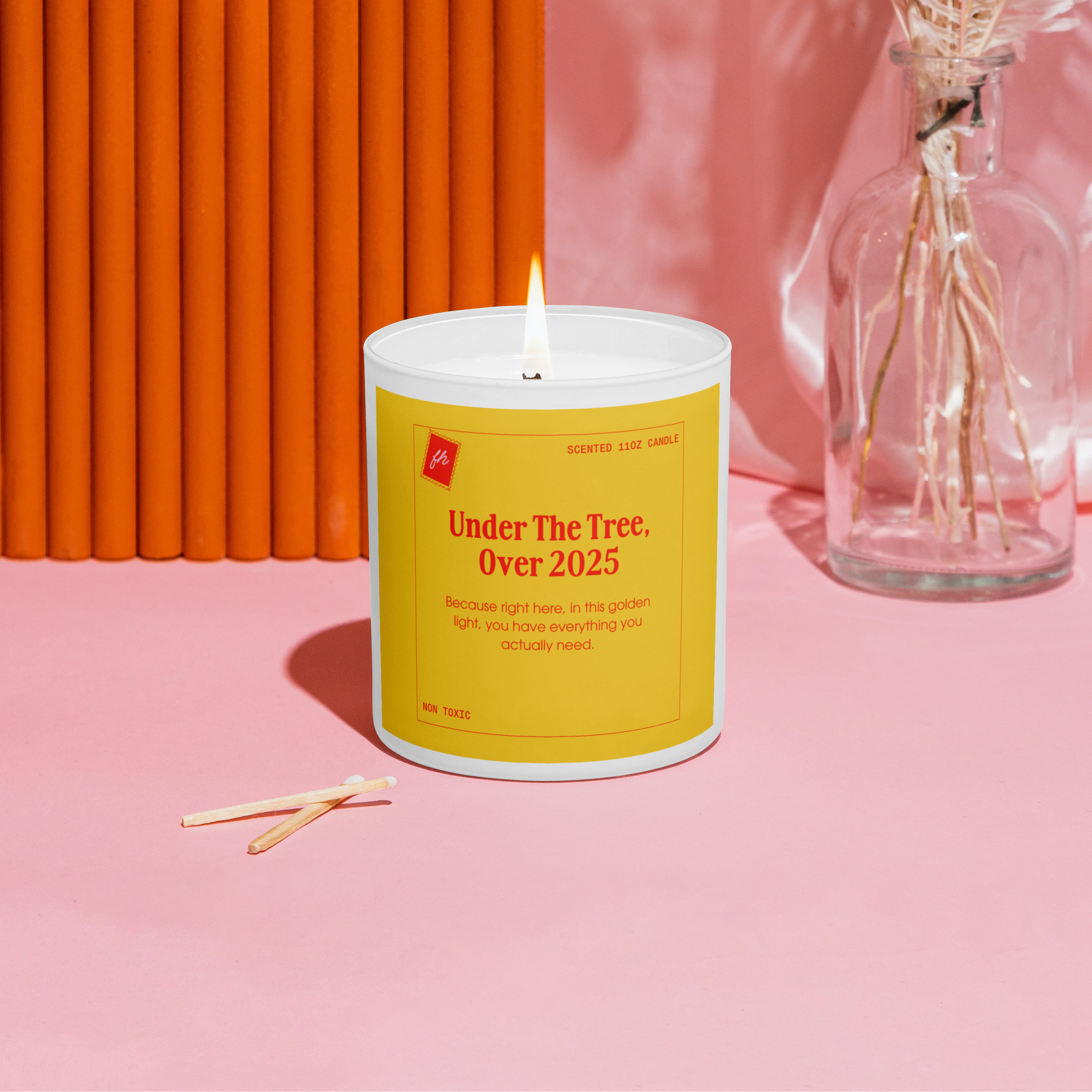 Candle with a yellow label on a pink surface with an orange wall in the background
